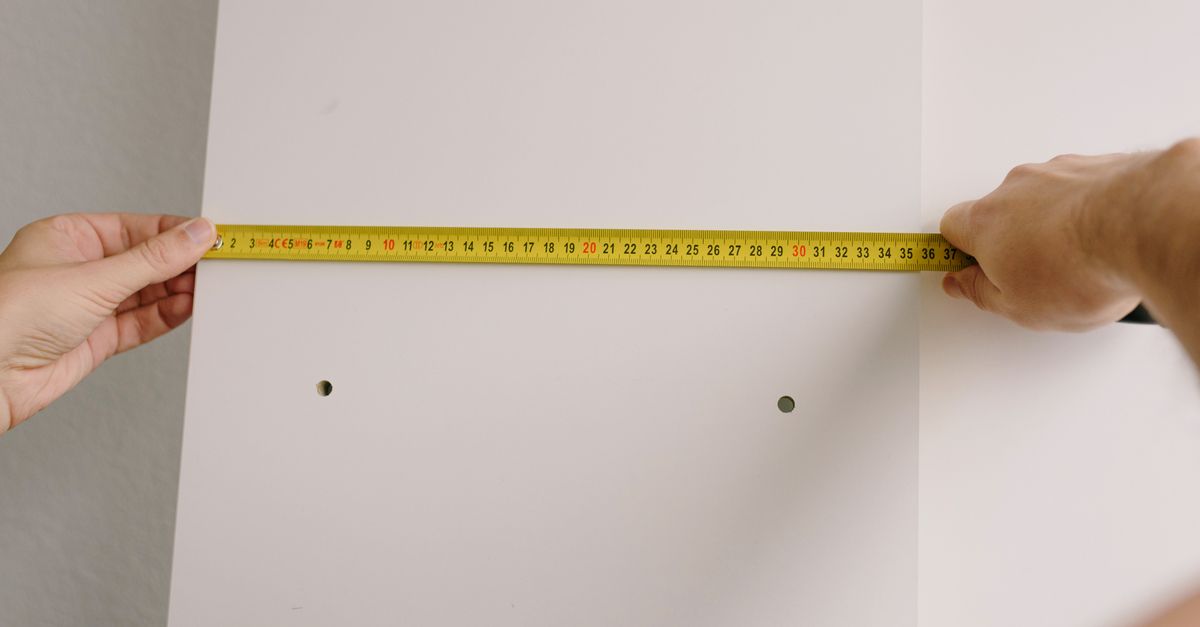 Crop unrecognizable male using measuring tape to make marks on white wooden board