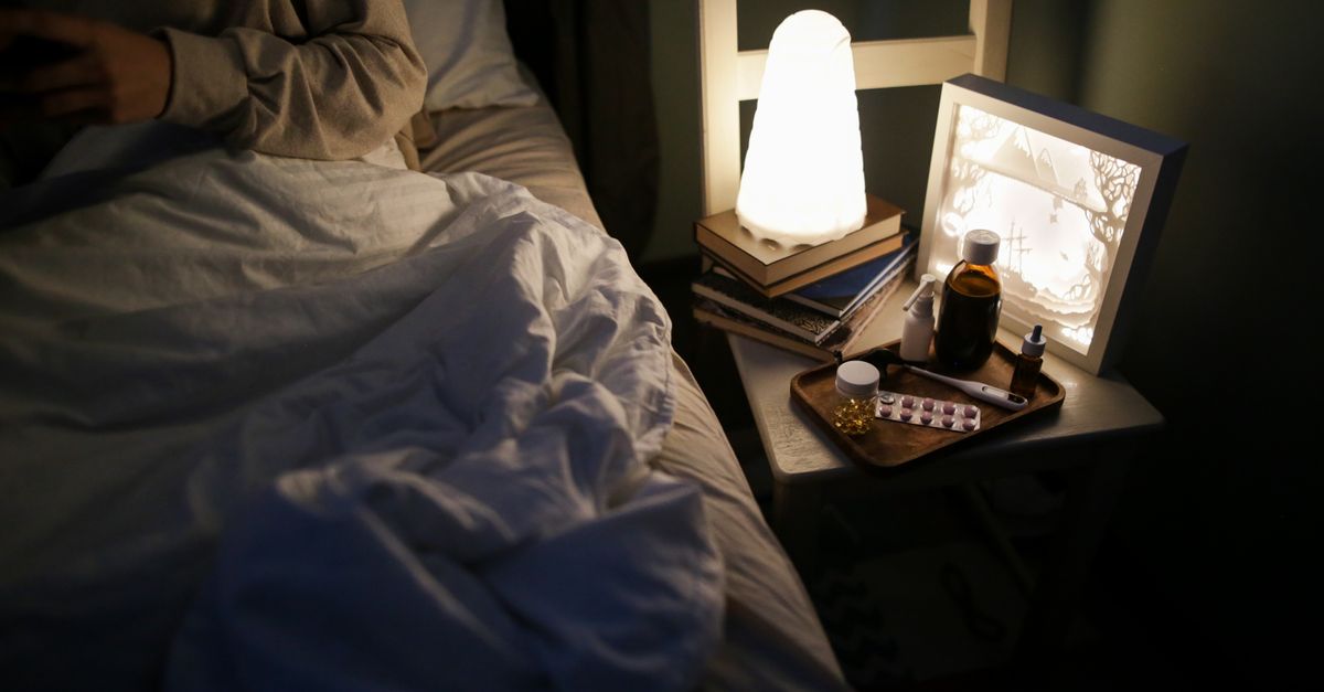 A bedside table with a lamp, books, and medicines for a cozy nighttime setting.