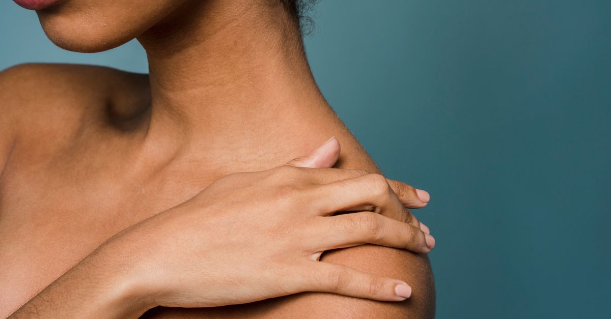 Side view of crop anonymous young graceful black female touching bare shoulder while standing against blue background