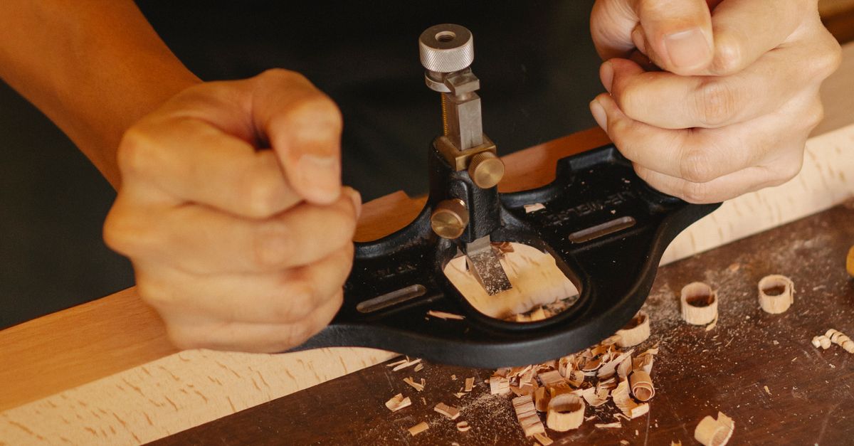 From above of crop anonymous male master preparing wooden detail with router plane in carpentry workroom