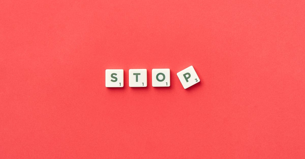 Scrabble tiles spelling 'STOP' on a vivid red background, viewed from above.