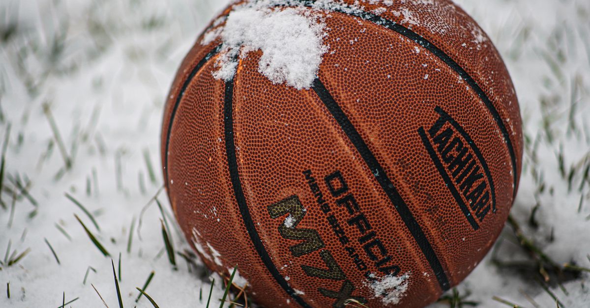 A close-up of a basketball resting on snow-covered grass, emblematic of winter outdoor sports.