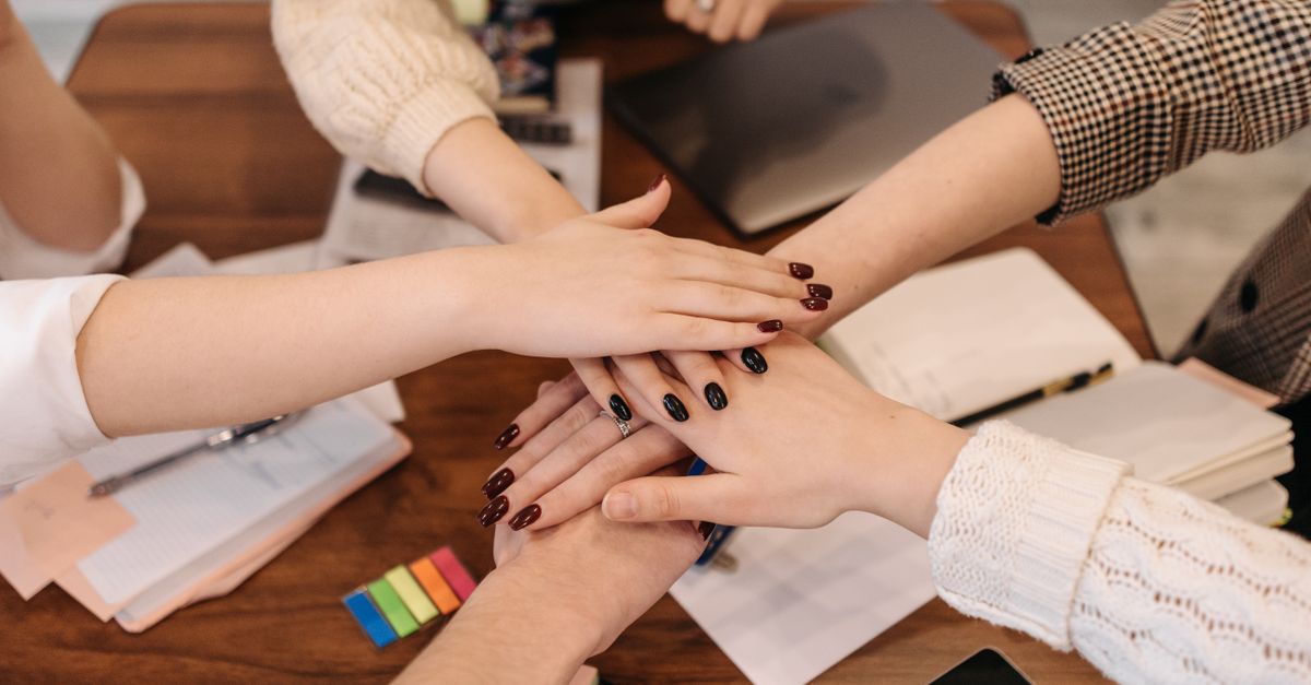 Hands stacked in teamwork gesture over a table with office items symbolizing collaboration.