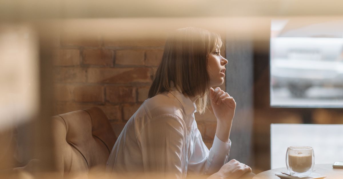 Reflective moment of a woman in a coffee shop by a window, enjoying a coffee.
