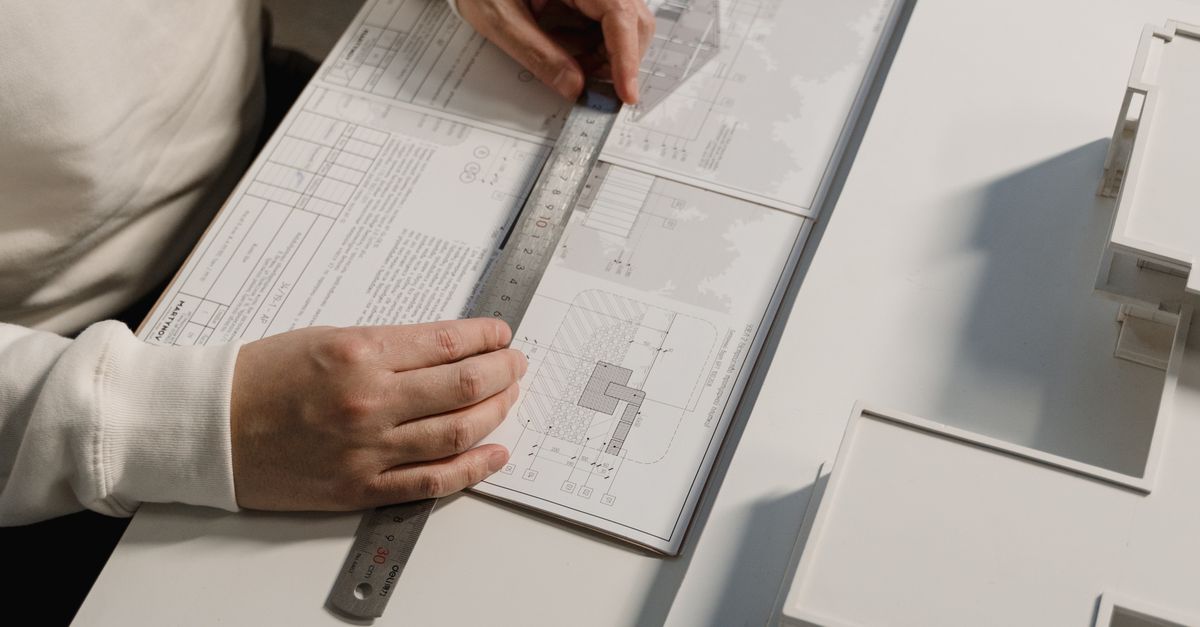 Hands of a person drafting architectural designs with a ruler on paper, indoors.
