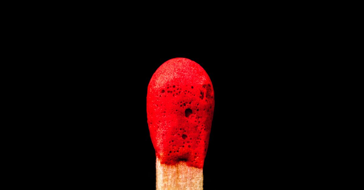 A detailed macro image of a match head against a stark black background, highlighting texture.