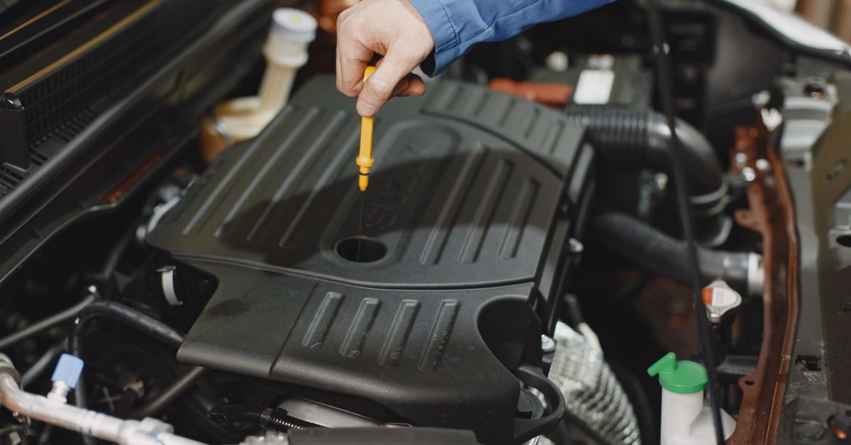 Close-up of a person checking engine oil using a dipstick in a car's engine bay.