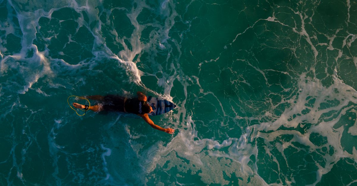 Dynamic aerial view of a surfer paddling through turquoise ocean waves, capturing the essence of ocean adventure.