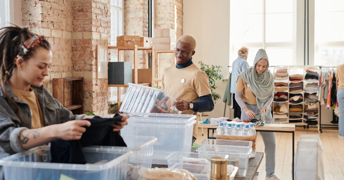 Group of diverse volunteers organizing donated clothing and supplies in a bright, airy warehouse.