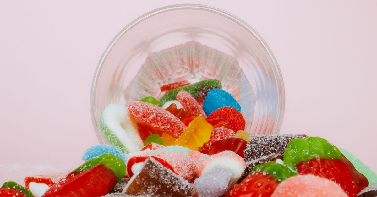 Vibrant sweet gummies spilling from a bowl on a pastel background.