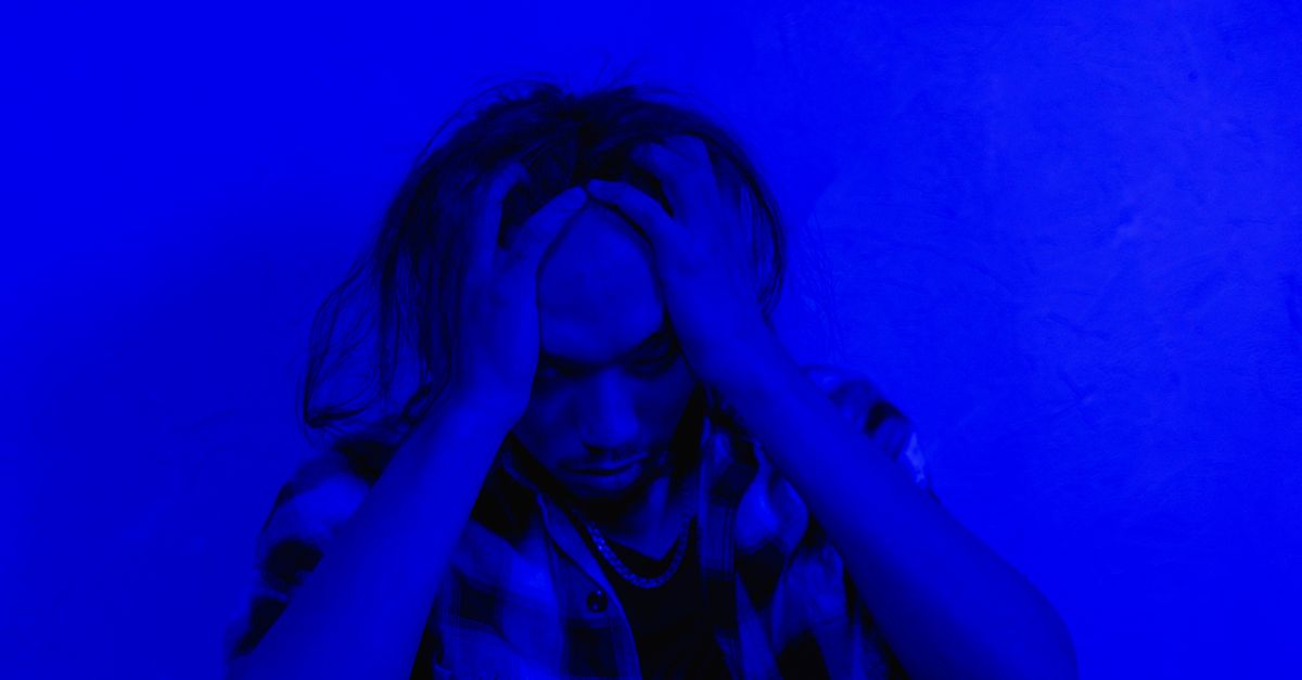 Portrait of a distressed person under dramatic blue lighting, expressing mental anguish.