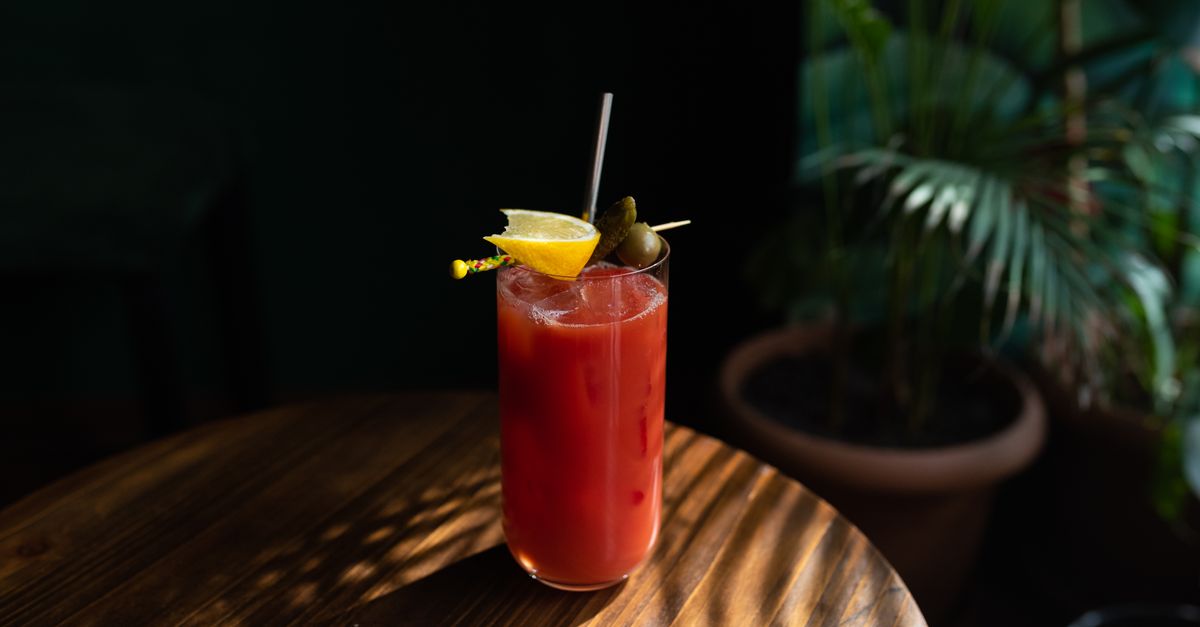 A vibrant Bloody Mary garnished with lemon and pickle, served in a tall glass.