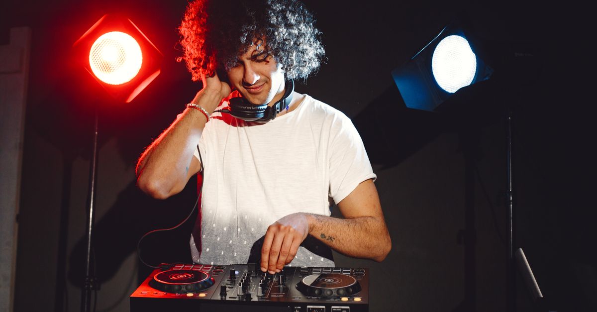 DJ with curly hair mixing music on a turntable in a vibrant club atmosphere.