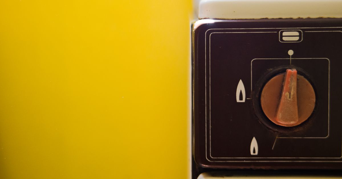 Close-up of a vintage gas stove knob on a vibrant yellow background.