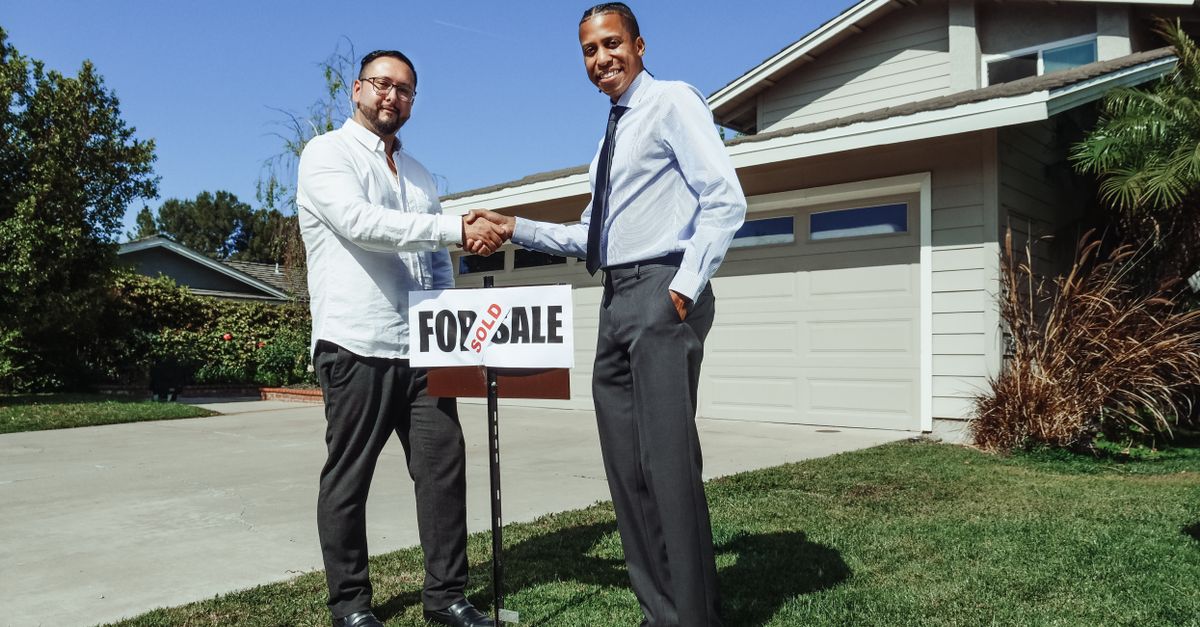 Two men shake hands in front of a new home with a sold sign, symbolizing a successful real estate deal.