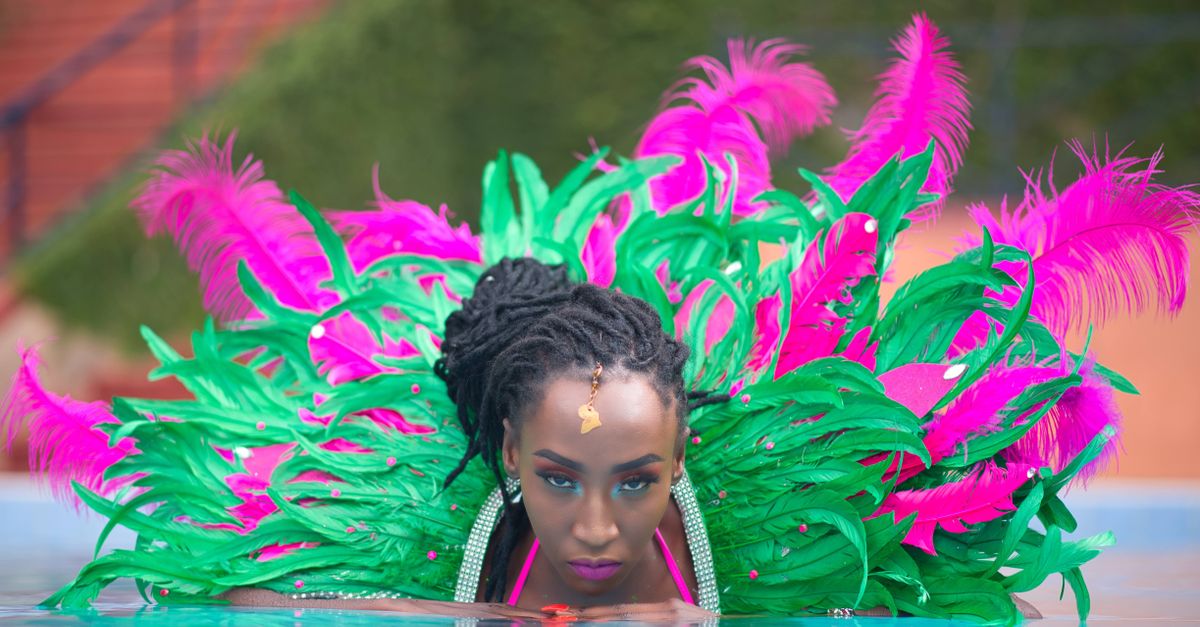 A stylish woman in a colorful feathered costume poses confidently in a pool setting.