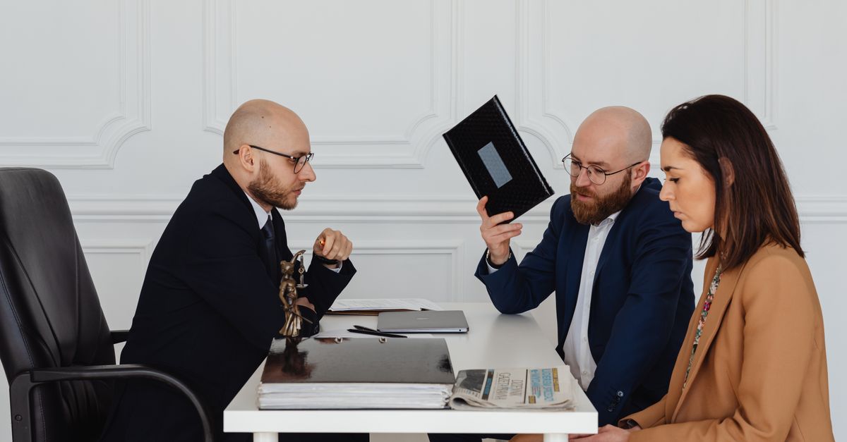 A couple in a legal consultation with a lawyer at an office desk.