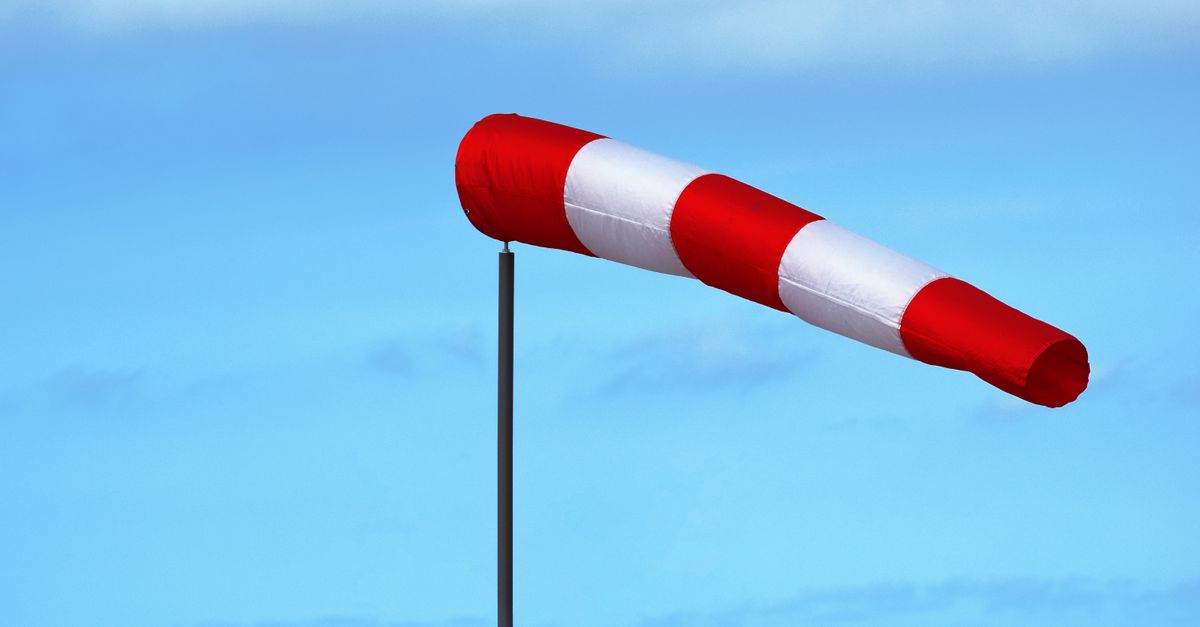 Red and white windsock indicating wind direction and speed against a clear blue sky.