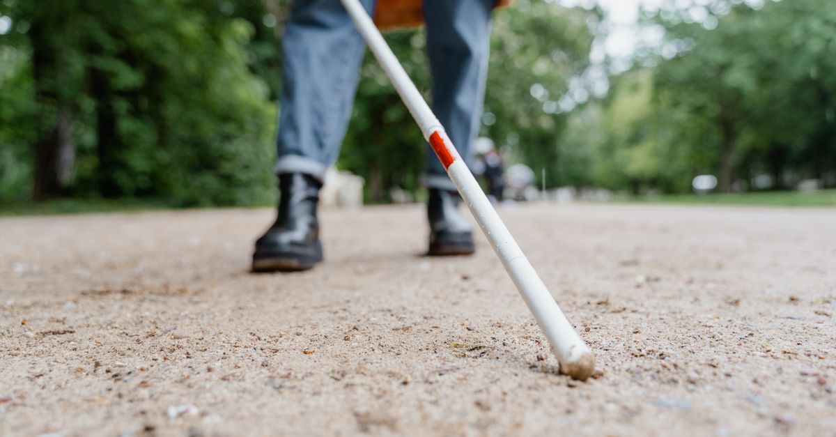 A person using a white cane to walk through a park, ensuring mobility and independence.