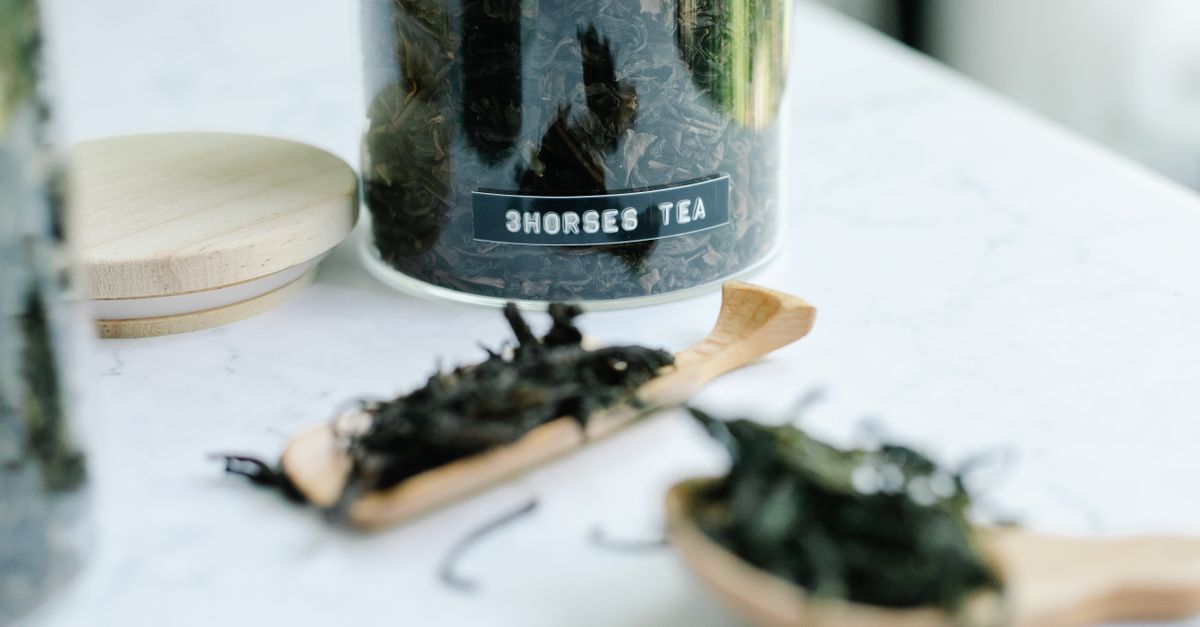 Detailed view of herbal tea stored in a glass jar with loose leaves on wooden spoons, highlighting a natural theme.