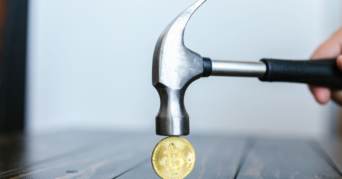 Close-up of a hammer poised above a Bitcoin coin on a wooden surface, representing cryptocurrency challenges.