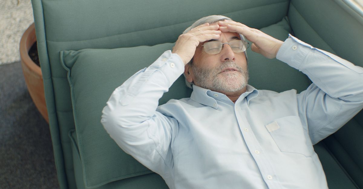 A senior man with eyeglasses relaxing on a sofa, looking stressed and tired.