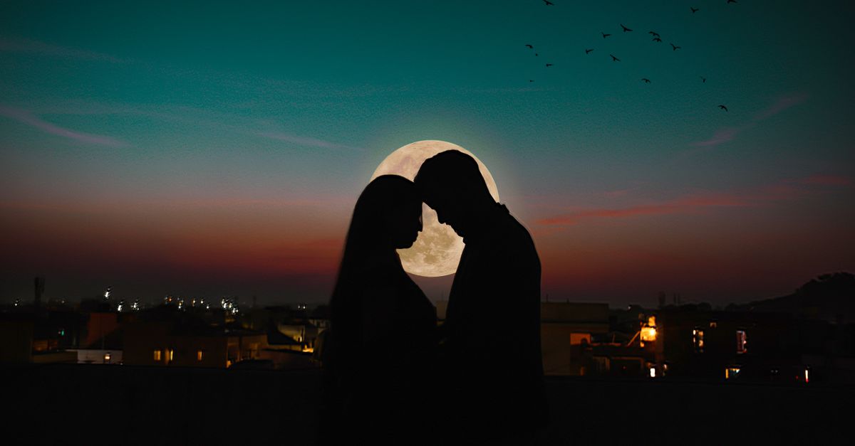 Silhouette of a couple in love under a full moon with a dramatic night sky.