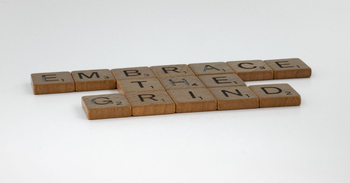 Scrabble tiles on a white background forming the motivational phrase 'Embrace the Grind'.