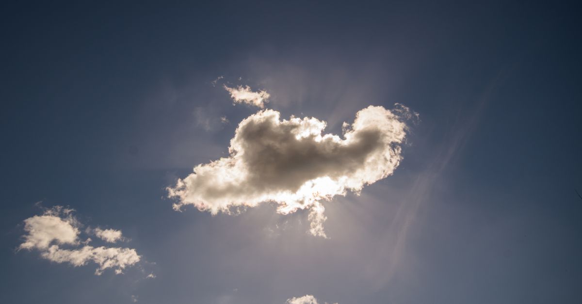 A beautiful scene of sunlight streaming through a fluffy cloud against a clear blue sky.