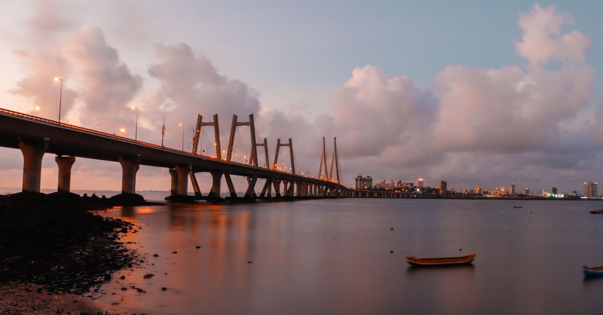 A breathtaking evening view of a bridge extending over calm waters, with city skyline in the background.