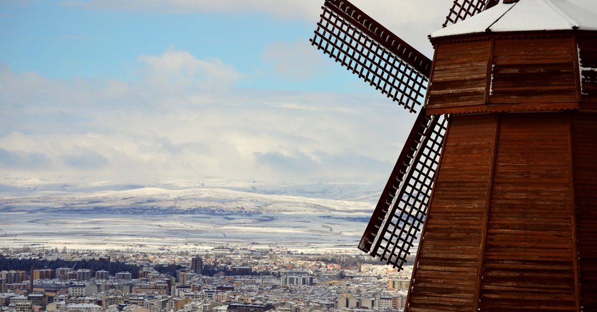 A picturesque view of a snow-covered city with a wooden windmill, set against a winter landscape.