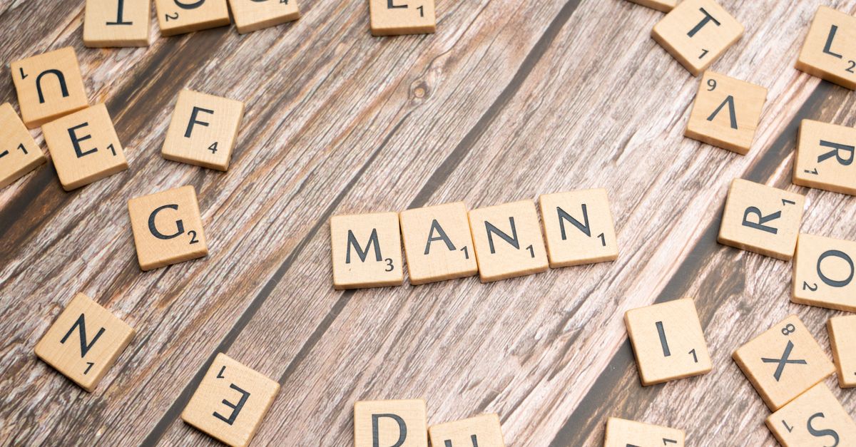 Wooden letter tiles forming the word 'MANN' on a rustic wooden table background.
